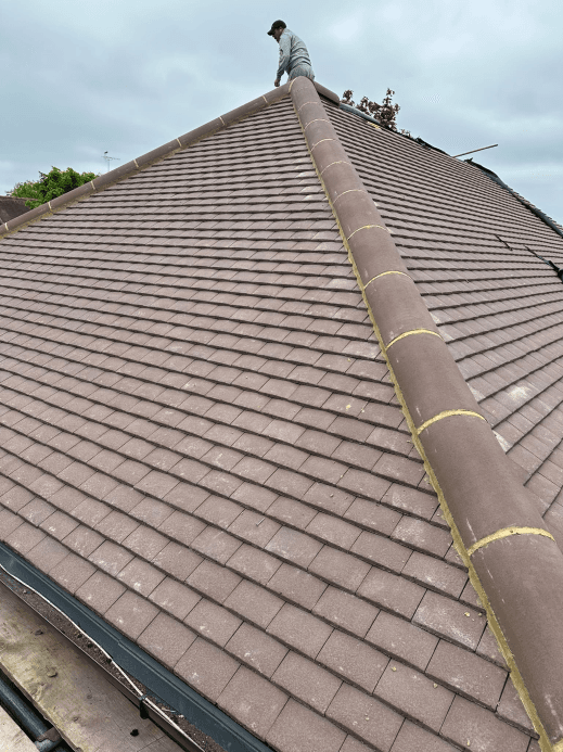 Clay tiled roof with ridge work and workman on top